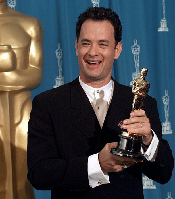 Tom Hanks sonriendo en la entrega de lso premios óscar y sosteniendo una estatuilla ganadora
