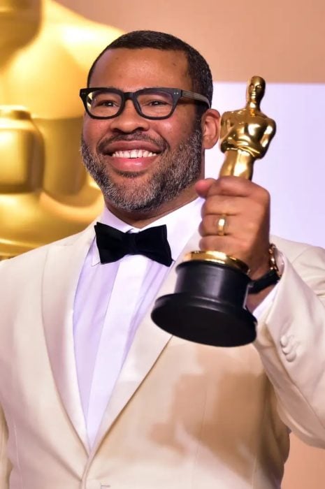 Jordan Peele sosteniendo una estatuilla de los premios Óscar, llevando un saco dorado con camisa blanca