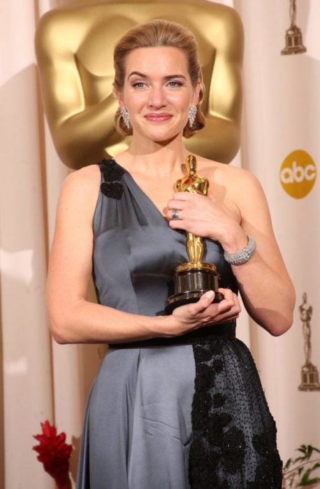 Kate Winslet so un vestido a tirantes anchos en tono gris sosteniendo una estatuilla a los premios Óscar