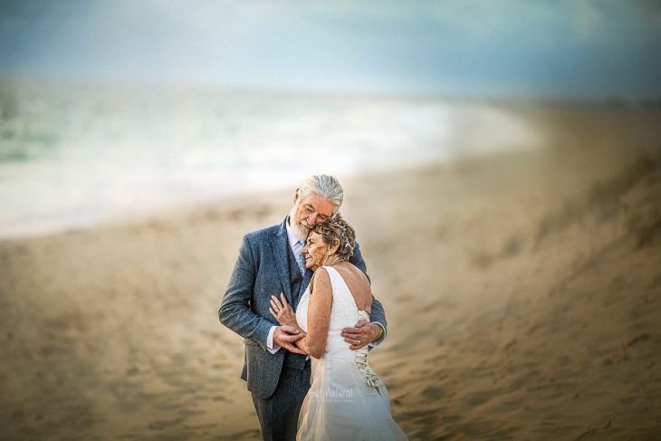 Fotografía por Abigail's Collection & The Groom's Room, pareja de abuelos abrazados en la playa mirando el mar