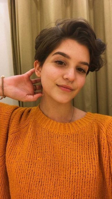 Chica con corte pixie y suéter naranja