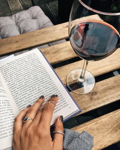 Mujer leyendo libro con copa de vino tinto