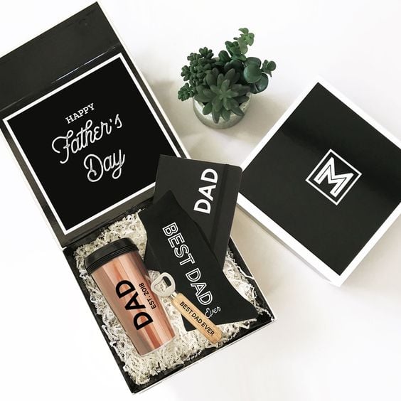 Caja de cartón negro rellena con un termo y tarjetas de felicitación del Día del padre