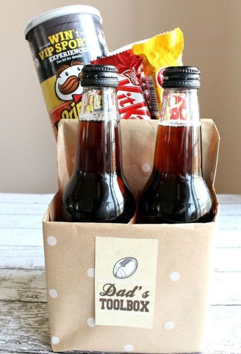 Caja de cartón con forma de six pack de cerveza llena de papas fritas y chocolates