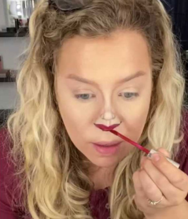 Mujer dibujando unos labios en la punta de la nariz con un color rojo