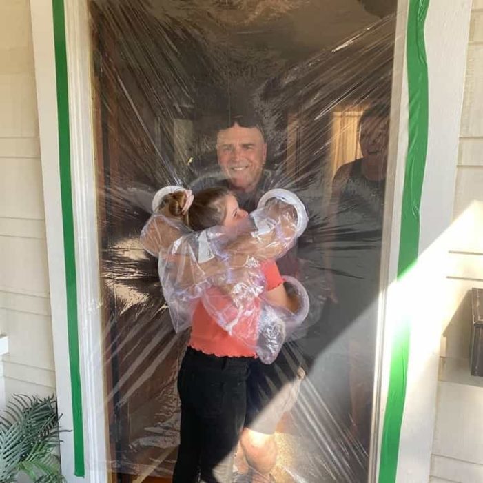 Niña abrazando a sus abuelos a través de una puerta de plástico 