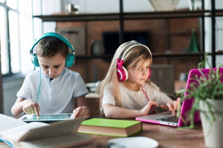 Niños rubios con audífonos grandes y tablets en clases online