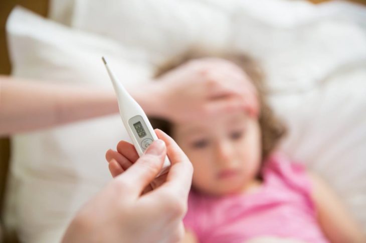 Niña recostada en cama y su mamá tomándole la temperatura 