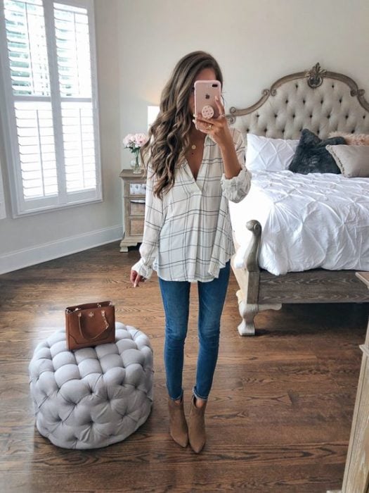 Chica de cabello largo y rizado se toma selfie frente al espejo con blusa a cuadros delgada con jeans