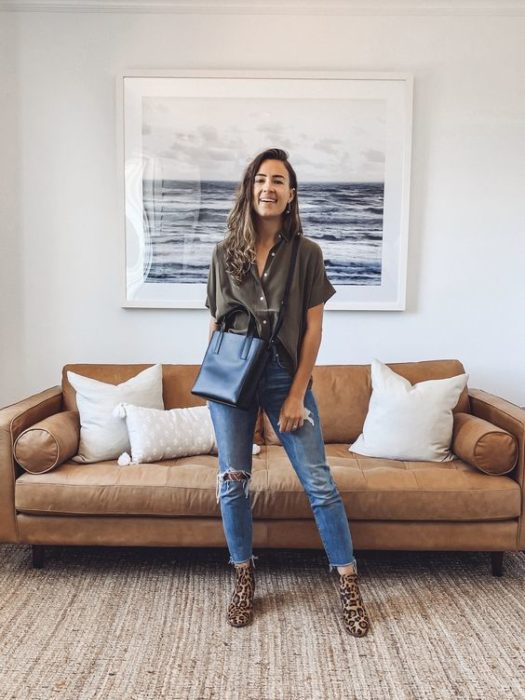 Chica posa en la sala de su casa con jeans, bolsa negra grande y blusa verde