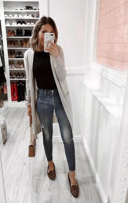Mujer de melena corta se toma selfie con cardigan gris, blusa negra y jeans