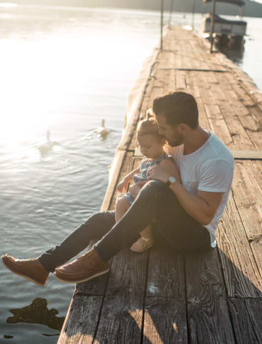 Frases del día del padre; papá e hija sentados a la orilla de un lago