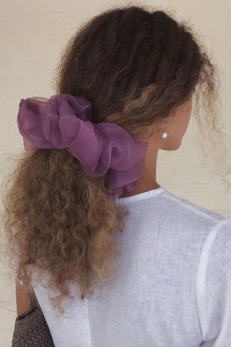 Chica rizada con coleta abajo y un scrunchie gigante morado