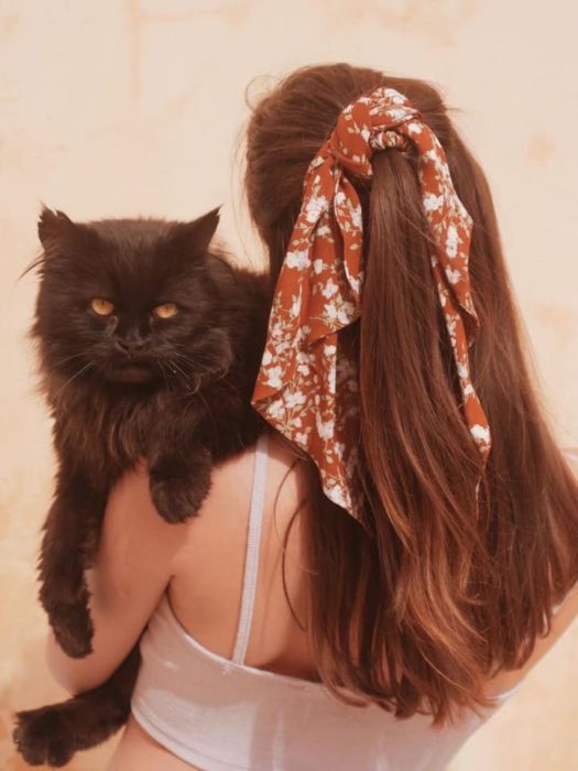 Chica de pelo largo recogido en media cola con una pañuelo naranja abraza a un gato negro