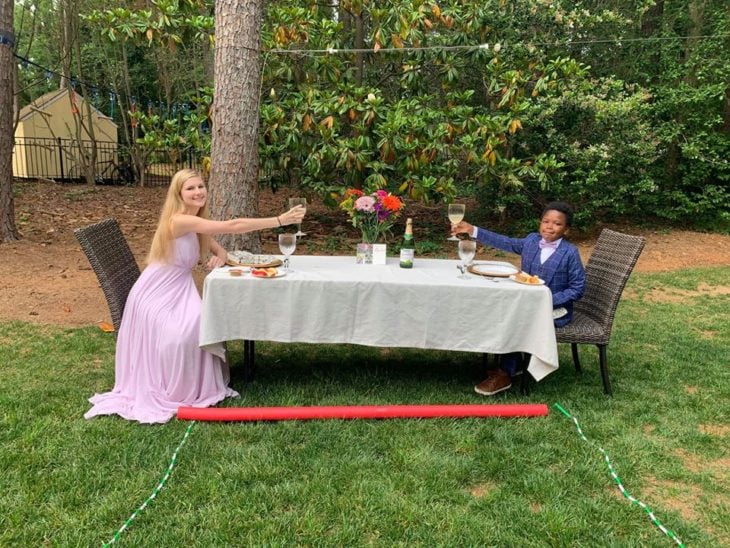 Chica y un niño comiendo en una mesa de jardín larga con un mantel blanco