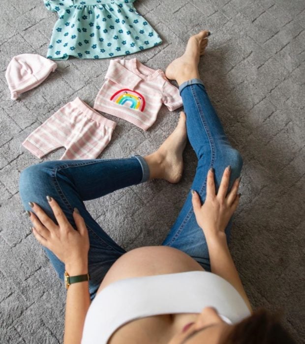 Mujer embarazada mostrando ropita de su bebé