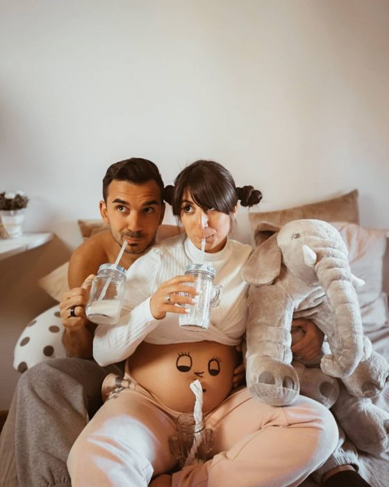 Pareja embarazada haciéndose una foto graciosa en la que los 3 toman leche