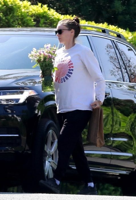 Rooney Mara con sudadera holgada bajando de una camioneta negar con una ramo de flores en la mano