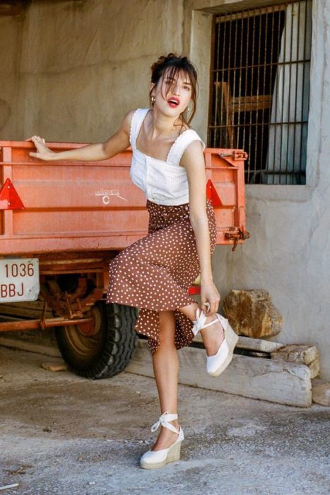 Chica con falda larga de flores y blusa blanca con tacones de cuña