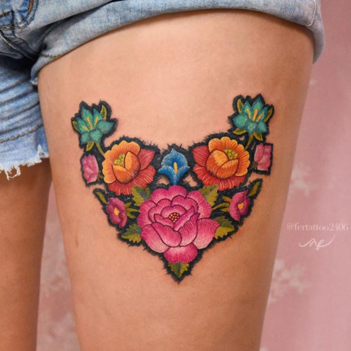 Fernanda Ramírez, tatuadora mexicana crea tatuajes bordados; flores rosas, azules y anaranjadas en la pierna