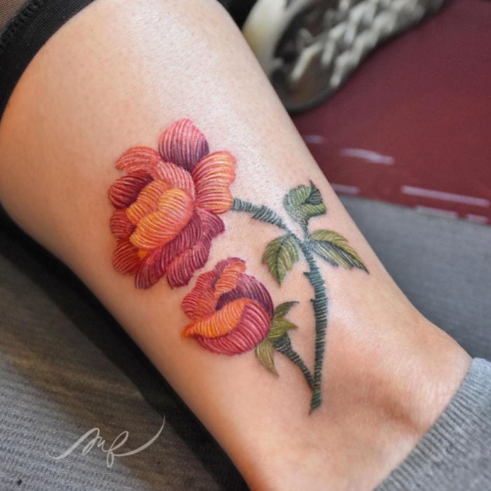 Fernanda Ramírez, tatuadora mexicana crea tatuajes bordados; flores anaranjadas en la pierna
