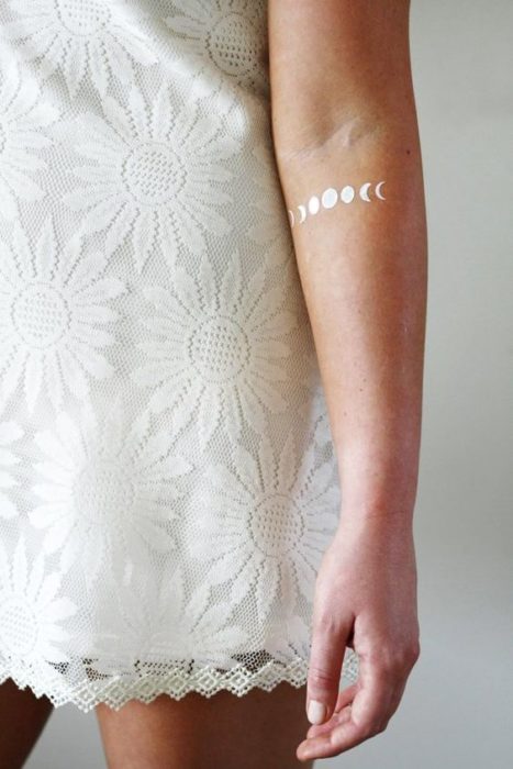 Tatuaje de fases lunares en el brazo con tinta blanca