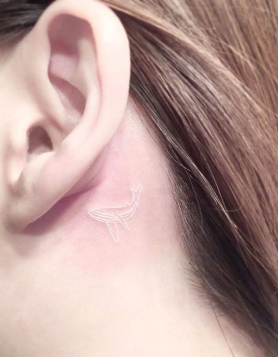 Tatuaje detrás de la oreja de una ballena hecho con tinta blanca