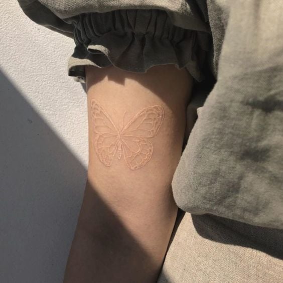 Tatuaje de mariposa en el brazo con tinta blanca