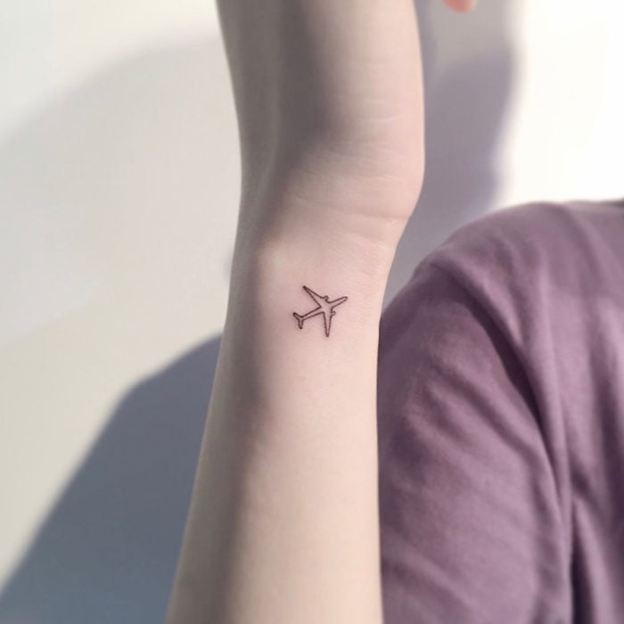 Tatuajes pequeños en la muñeca; silueta de avión