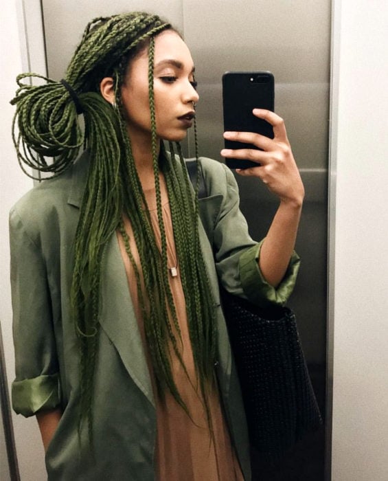 Looks con trenzas africanas; mujer morena de cabello largo y verde, arete en la nariz, estilo bohemio, tomándose selfie frente a espejo en elevador
