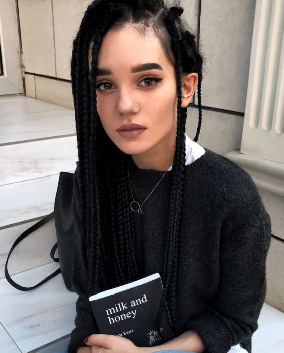 Looks con trenzas africanas; mujer con orejas de elfo, pecas, cabello negro y largo, sosteniendo un libro de Rupi Kaur, Milk and honey