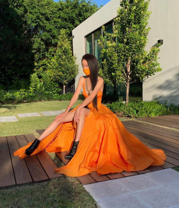 Vera Wang presume abdomen de acero; mujer sentada en el jardín con largo vestido anaranjado de princesa