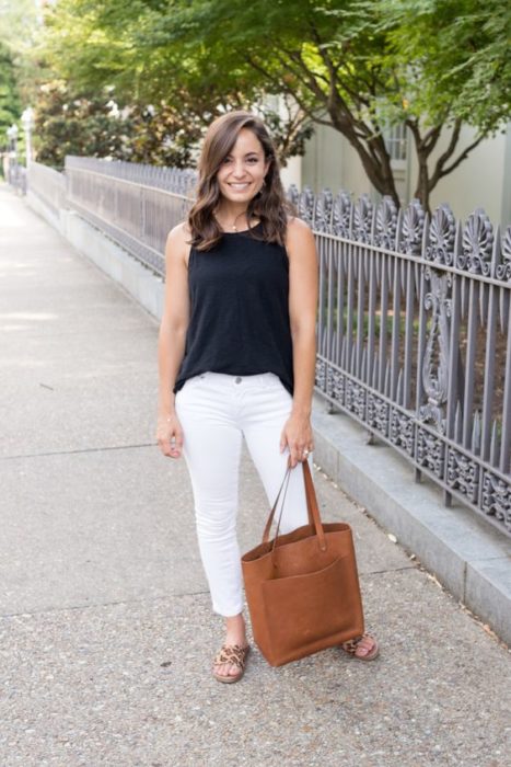 Mujer con bolsa grande color café usa blusa negra y pantalón blanco con sandalias animal print