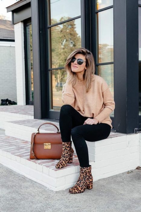 Mujer rubia con melena corta sentada con jeans, suéter rosa y botines animal print