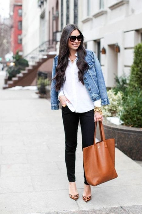 Chica de pelo negro largo posa con pantalón negro, blusa blanca y chamarra de mezclilla