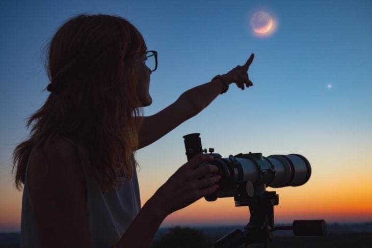 Chica mirando la luna y las estrellas por un telescopio