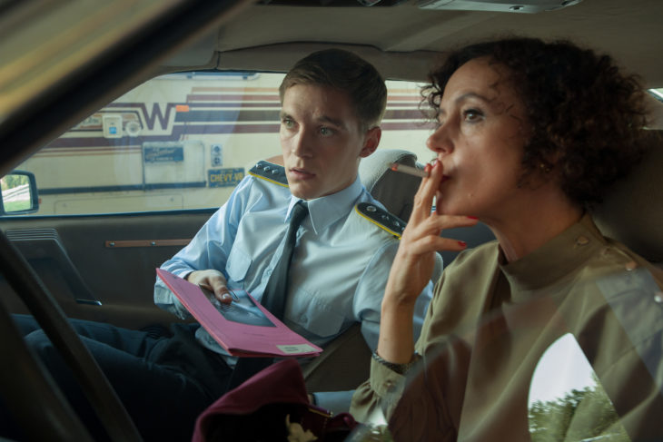 Escena de la serie Deutschland 83, mujer y un hombre fumando dentro de un automóvil, espiando a su alrededor