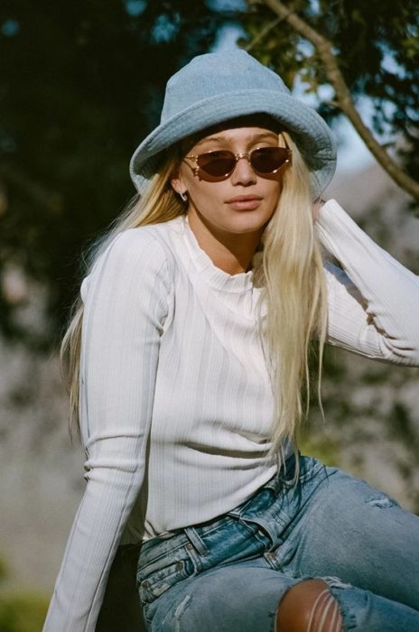 Chica llevando sombrero pescador de mezclilla azul cielo y gafas cafés