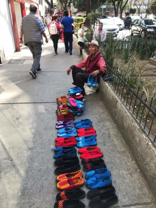 Abuelito sentado en la orilla d euna pileta vendiendo zapatos de colores