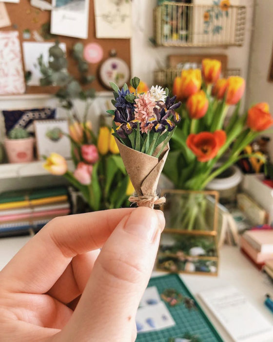 Miniramo de flores de papel de la artista Tania Lissova con flores en tonso morados envuelta en un cartoncillo café