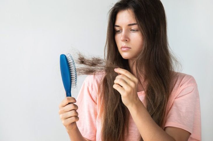 Chica sosteniendo un cepillo azul lleno de cabello