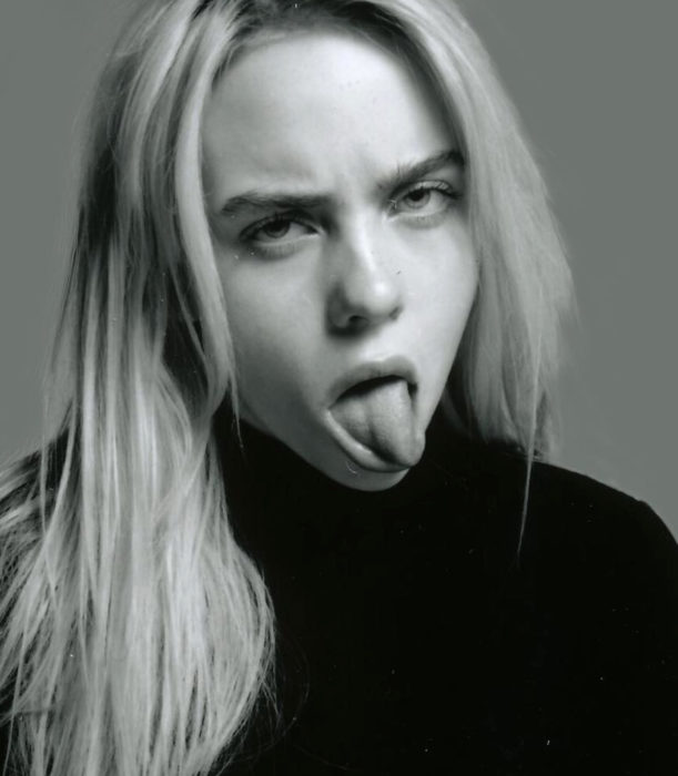 Fotografía en blanco y negro de Billie Eilish sacando la lengia, con cabello suelto