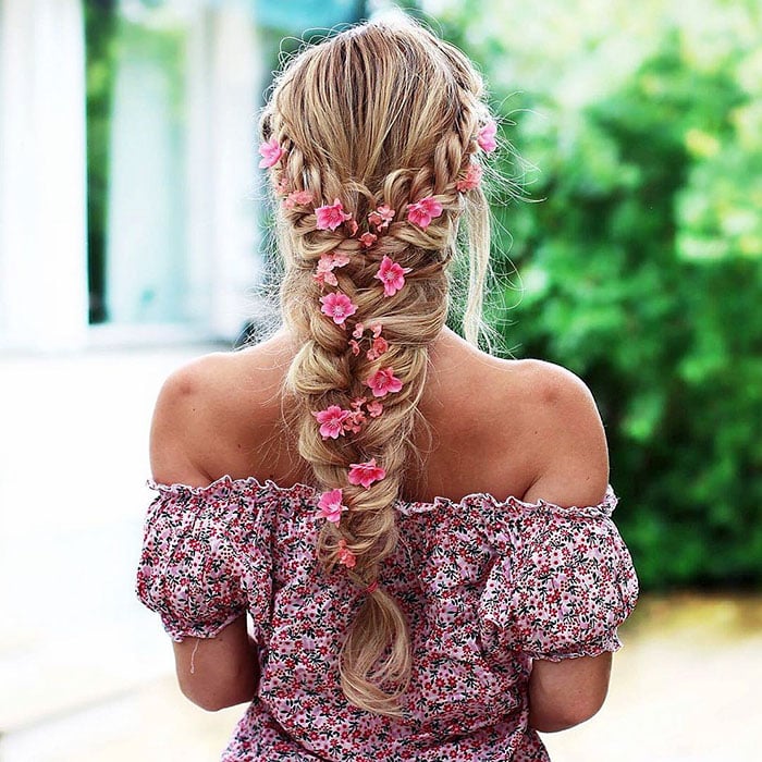 Chica rubia de cabello largo con trenza esponjosa con flores rosas