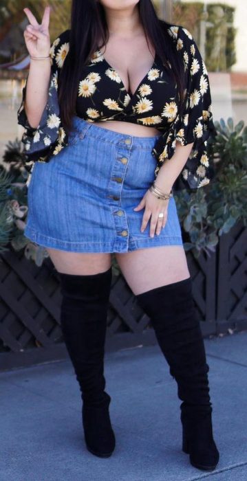 Chica curvy con falda de mezclilla, botas negras altas y blusa negra con flores