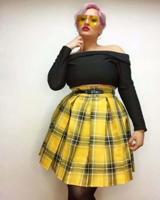 Modelo plus size posa con blusa sin hombros negra y falda de cuadros a amarilla