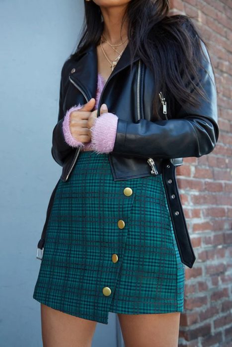 Chica usando chaqueta de cuerto, suéter rosa y falda verde de cuadros