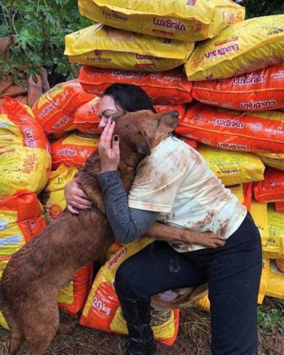 Mujer siendo abrazada por un perro al que llevó bultos de alimento