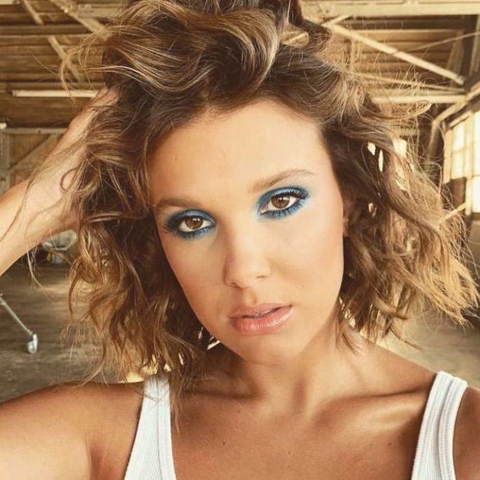 Millie Bobby Brown con el cabello teñido de color rubio y un maquillaje en colores turqueza 