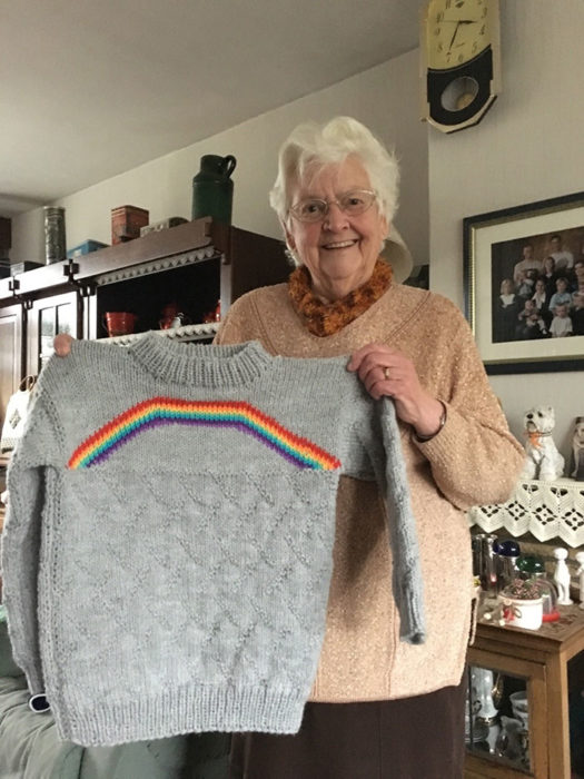 Mujer sosteniendo un sueter de color gris tejido con un arcoíris del orgullo Lgbtq