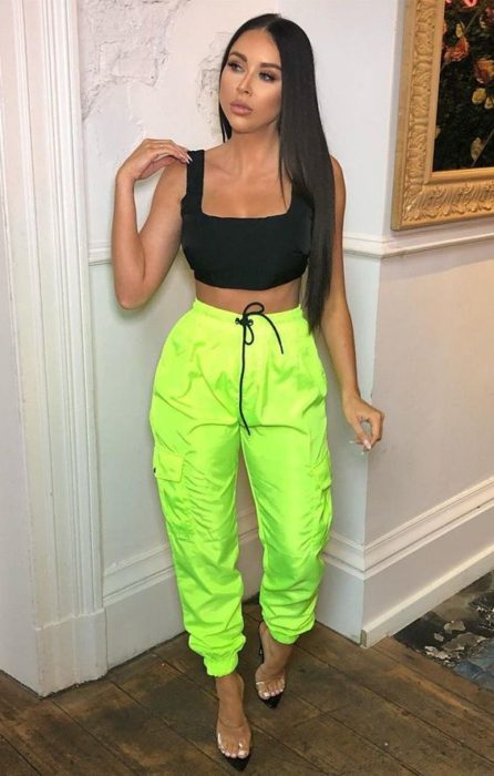 Chica morena de cabello largo con top negro y pantalón verde neón